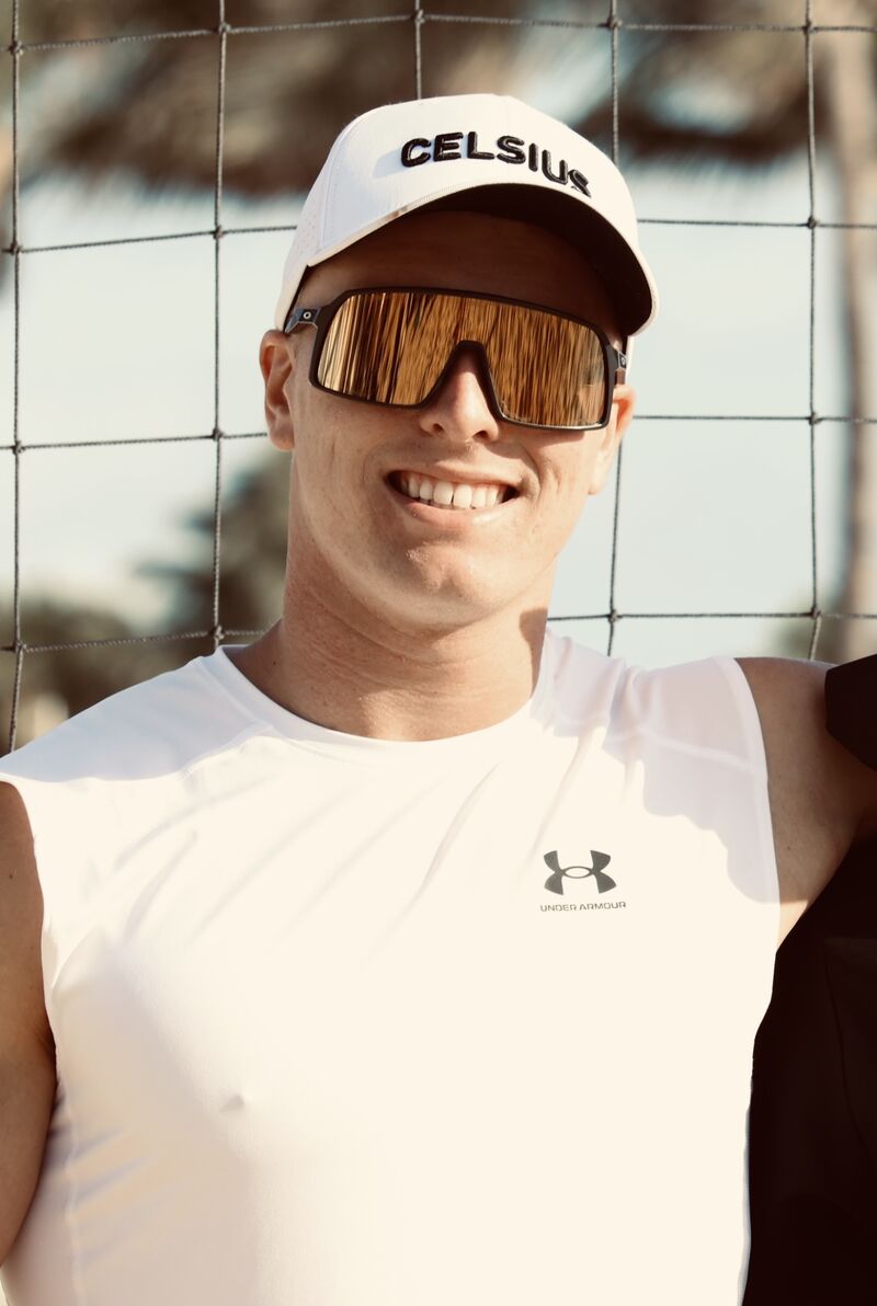 Coach Aidan Patterson smiling in a white cap and sport sunglasses